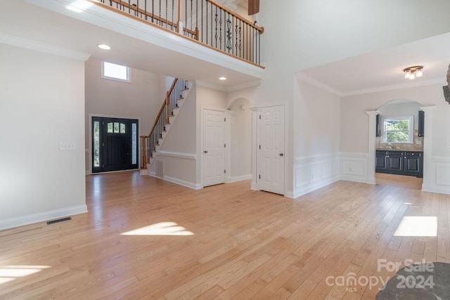 foyer entrance featuring crown molding, a towering ceiling, and light wood-type flooring