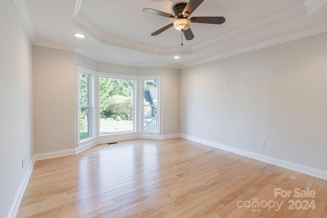 spare room with a tray ceiling, ceiling fan, ornamental molding, and light wood-type flooring