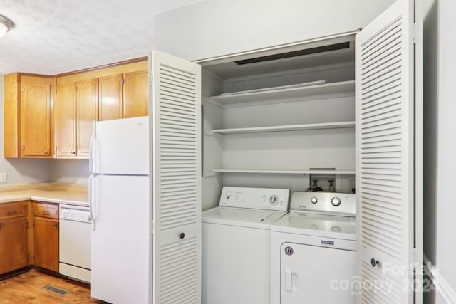 clothes washing area with washing machine and clothes dryer, a textured ceiling, and light hardwood / wood-style floors