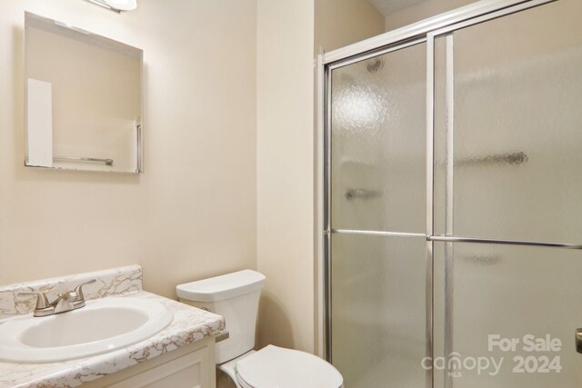 bathroom with a shower with door, vanity, and toilet