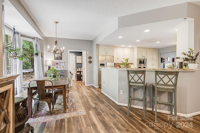 kitchen with a textured ceiling, dark hardwood / wood-style flooring, stainless steel fridge, kitchen peninsula, and light stone counters