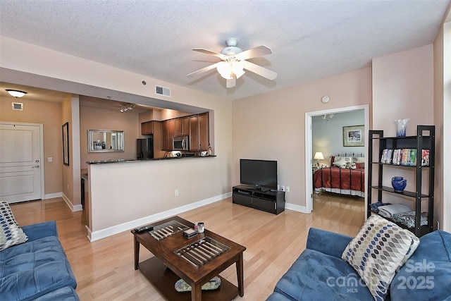 living room with ceiling fan, a textured ceiling, and light hardwood / wood-style flooring