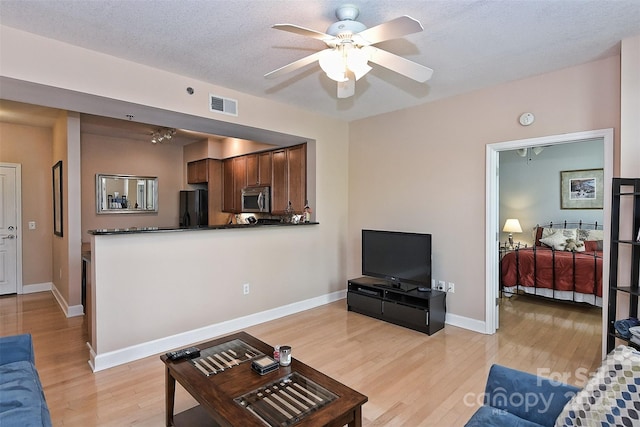 living room featuring ceiling fan, a textured ceiling, and light wood-type flooring