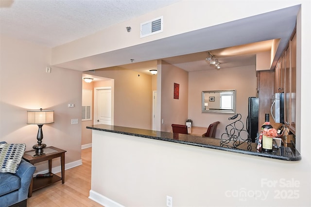 kitchen with refrigerator, kitchen peninsula, a textured ceiling, and light hardwood / wood-style flooring