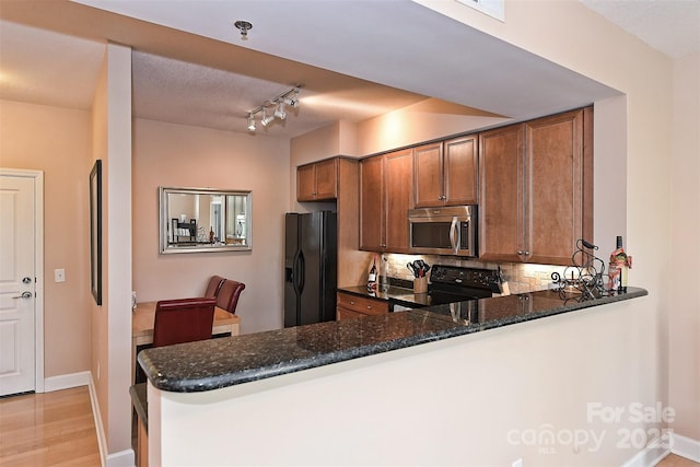 kitchen featuring backsplash, black appliances, dark stone countertops, light wood-type flooring, and kitchen peninsula