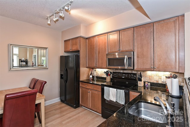 kitchen with dark stone counters, black appliances, sink, a textured ceiling, and light hardwood / wood-style floors