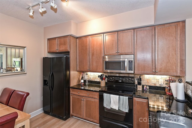 kitchen with a textured ceiling, light wood-type flooring, dark stone countertops, and black appliances