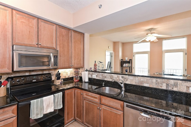 kitchen featuring appliances with stainless steel finishes, ceiling fan, dark stone counters, and sink