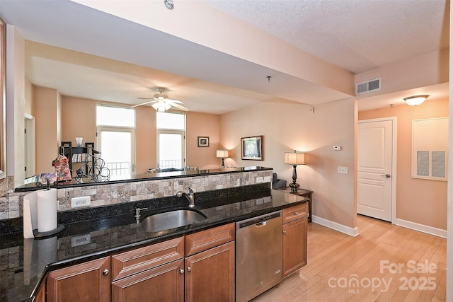 kitchen featuring ceiling fan, sink, stainless steel dishwasher, dark stone counters, and light wood-type flooring