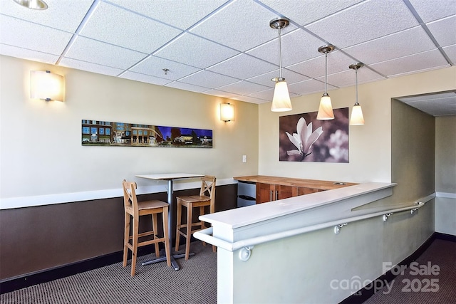 bar with dark colored carpet, a drop ceiling, and hanging light fixtures