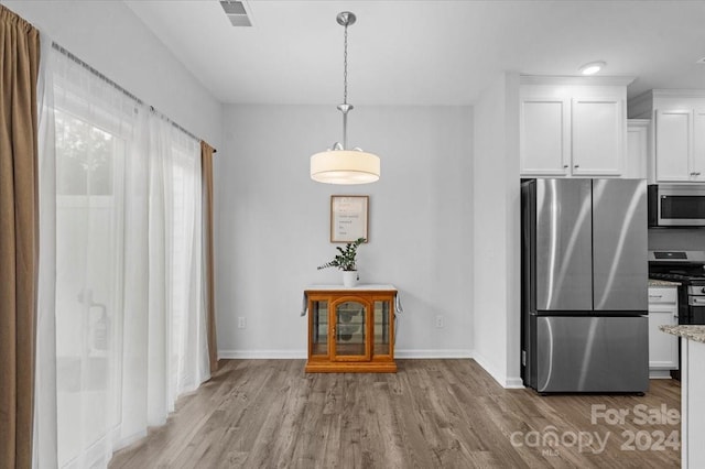 kitchen featuring appliances with stainless steel finishes, white cabinetry, hanging light fixtures, light stone counters, and light hardwood / wood-style flooring