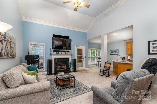 carpeted living room with high vaulted ceiling, a tiled fireplace, ornamental molding, sink, and ceiling fan