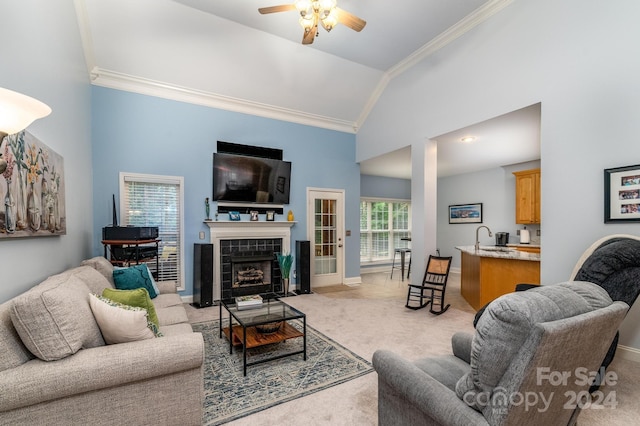 carpeted living room with a tiled fireplace, high vaulted ceiling, ornamental molding, and ceiling fan