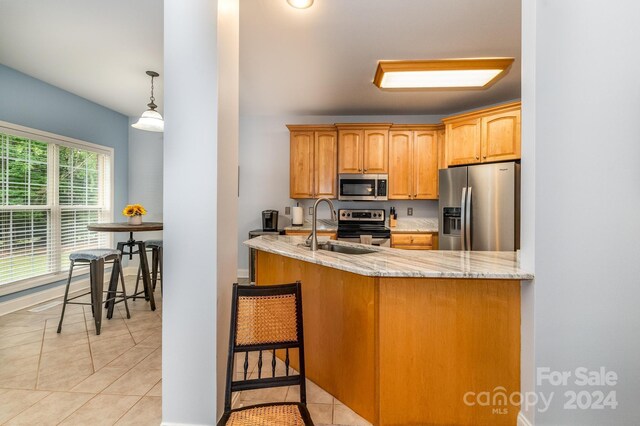 kitchen with light tile patterned floors, decorative light fixtures, light stone counters, stainless steel appliances, and a breakfast bar area