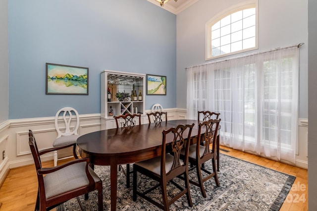 dining area featuring light wood-type flooring, crown molding, and a towering ceiling