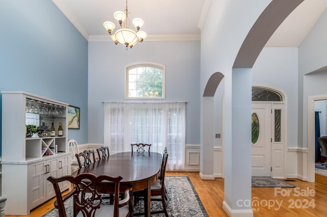 dining area with crown molding, a towering ceiling, a chandelier, and light hardwood / wood-style floors