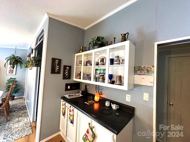 kitchen featuring a textured ceiling, ornamental molding, light hardwood / wood-style floors, and white cabinetry