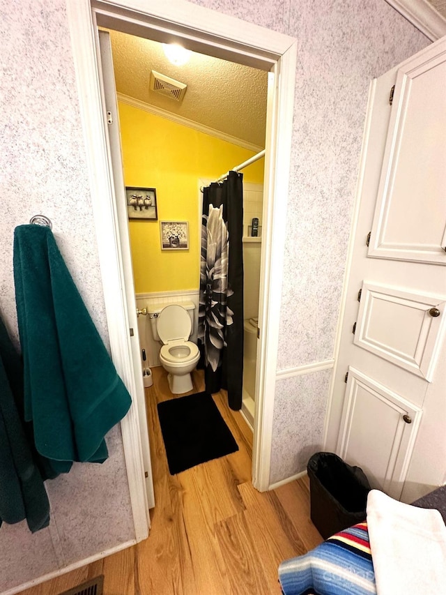 bathroom featuring toilet, hardwood / wood-style flooring, a textured ceiling, ornamental molding, and curtained shower