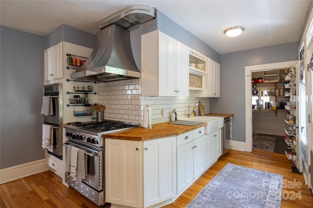 kitchen with white cabinets, stainless steel stove, butcher block counters, decorative backsplash, and light wood-type flooring