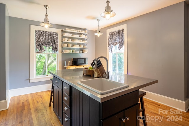 kitchen with a breakfast bar, light wood-type flooring, a center island, decorative light fixtures, and sink