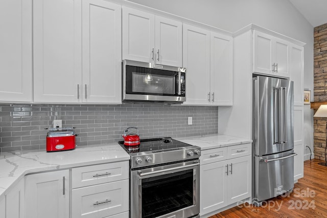 kitchen with white cabinets, vaulted ceiling, light hardwood / wood-style floors, light stone counters, and stainless steel appliances