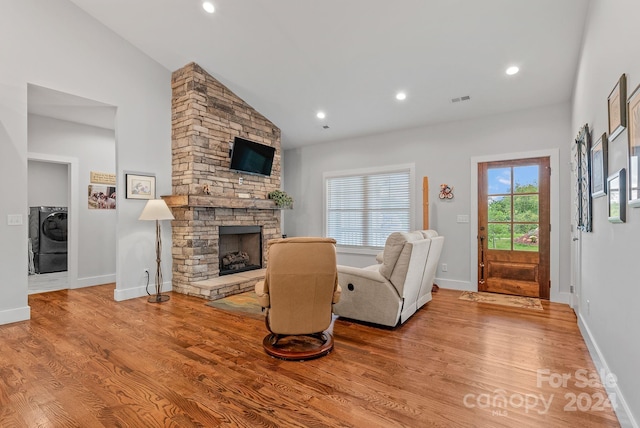 living room with a fireplace, washer / dryer, light wood-type flooring, and lofted ceiling