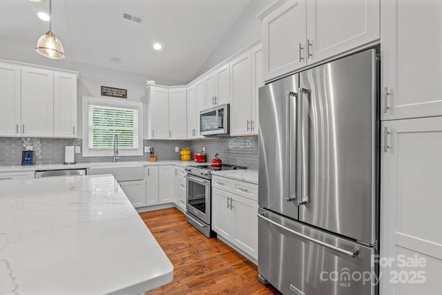 kitchen featuring white cabinetry, vaulted ceiling, visible vents, wood finished floors, and premium appliances