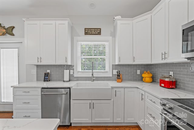 kitchen featuring stainless steel appliances, white cabinetry, a sink, and backsplash