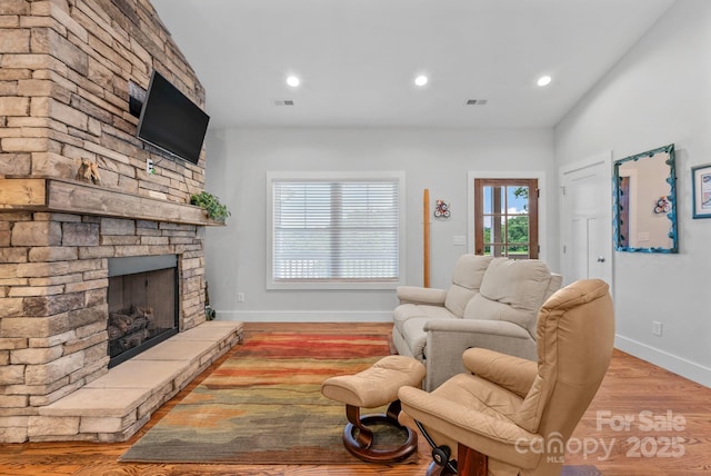 living area with visible vents, a stone fireplace, baseboards, and wood finished floors