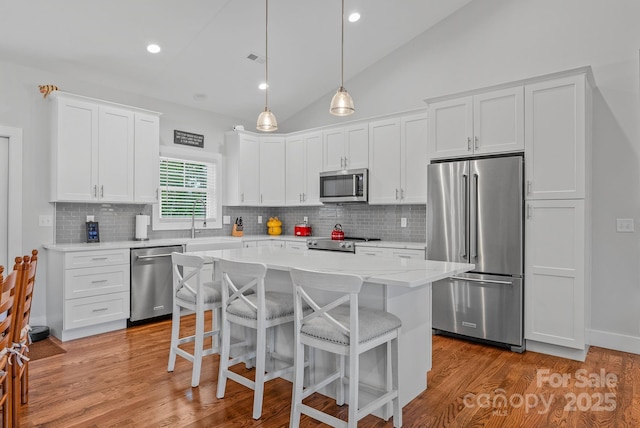 kitchen with lofted ceiling, a breakfast bar, white cabinetry, and appliances with stainless steel finishes