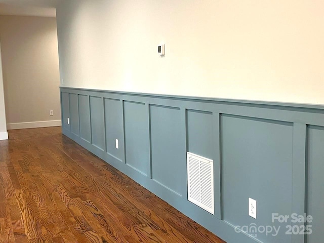 unfurnished room featuring dark wood-type flooring, visible vents, a decorative wall, and wainscoting