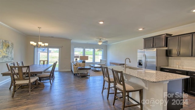 kitchen with dark hardwood / wood-style flooring, pendant lighting, stainless steel fridge with ice dispenser, an island with sink, and crown molding