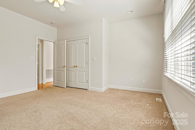 unfurnished bedroom with a ceiling fan, light colored carpet, visible vents, and baseboards