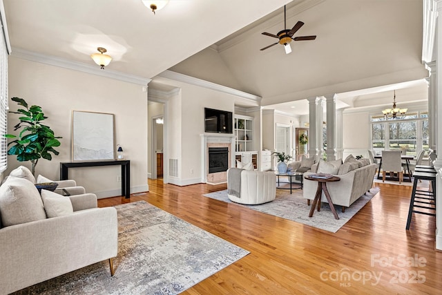 living area featuring ceiling fan with notable chandelier, a fireplace, wood finished floors, ornate columns, and crown molding