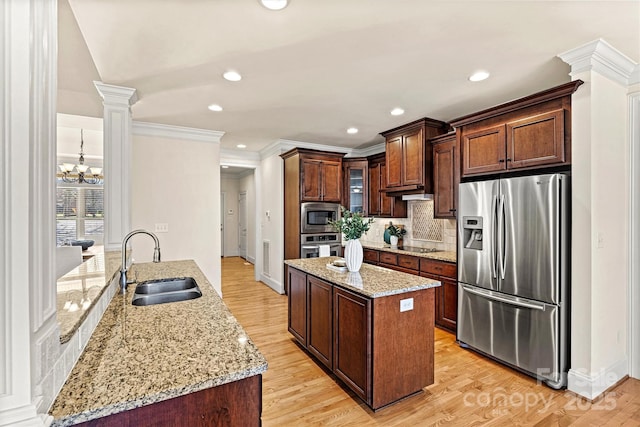 kitchen featuring light stone counters, decorative columns, appliances with stainless steel finishes, glass insert cabinets, and a sink