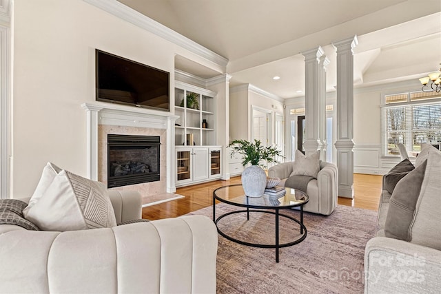 living room with built in shelves, decorative columns, ornamental molding, a high end fireplace, and wood finished floors