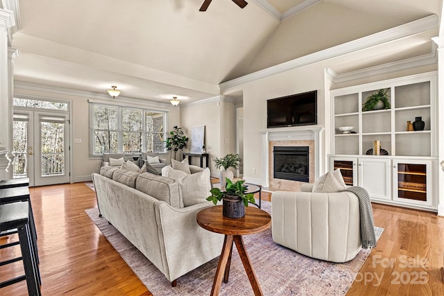 living room featuring ornamental molding, light wood-type flooring, vaulted ceiling, and a premium fireplace