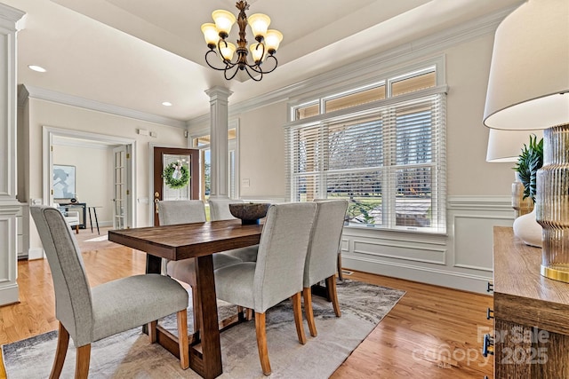 dining space featuring ornamental molding, a decorative wall, decorative columns, and light wood-style floors