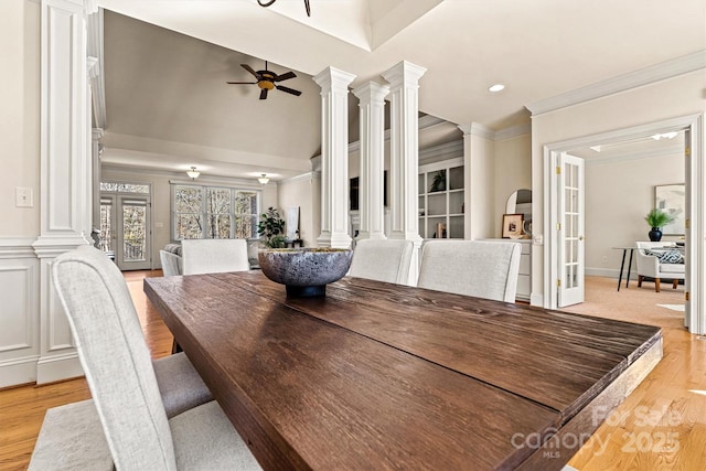 dining room featuring a towering ceiling, light wood-style floors, a ceiling fan, decorative columns, and crown molding