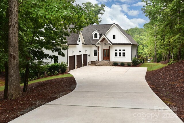 modern farmhouse featuring a garage, driveway, board and batten siding, and roof with shingles