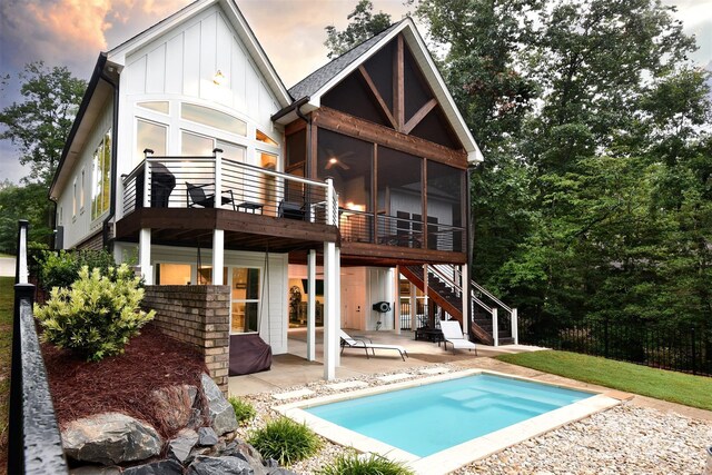 back of house at dusk featuring a fenced in pool, a patio, a sunroom, stairs, and board and batten siding