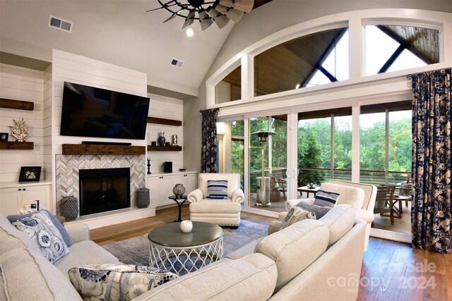 living room with high vaulted ceiling, a fireplace with raised hearth, visible vents, and wood finished floors