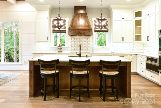 kitchen featuring light countertops, glass insert cabinets, custom exhaust hood, and a kitchen island with sink