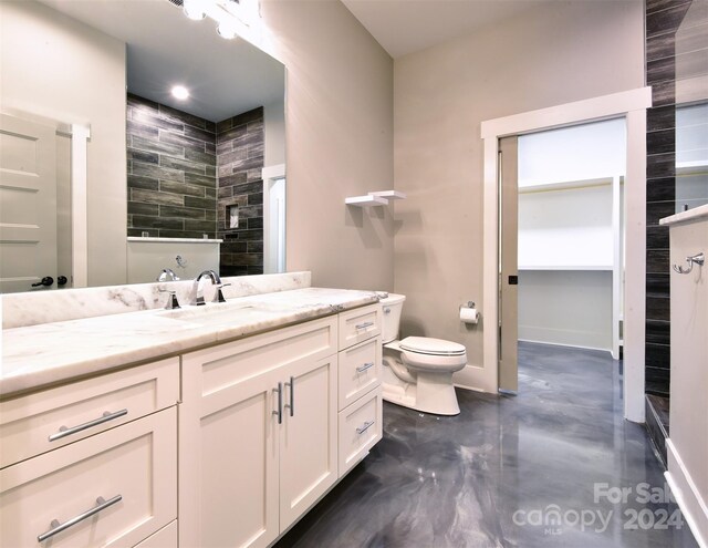 bathroom featuring toilet, a walk in closet, vanity, and baseboards