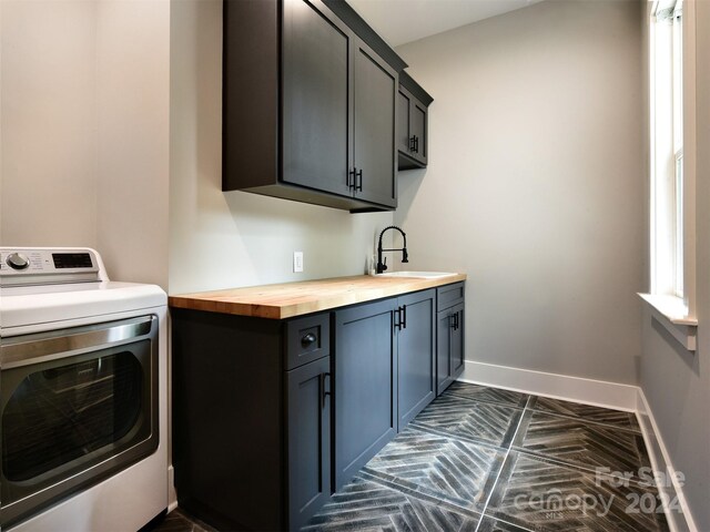 clothes washing area featuring cabinet space, a sink, washer / dryer, and baseboards