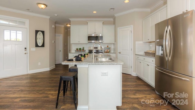 kitchen with white cabinetry, appliances with stainless steel finishes, a center island with sink, and tasteful backsplash