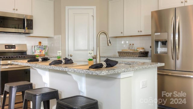 kitchen with a breakfast bar, white cabinets, stainless steel appliances, and tasteful backsplash