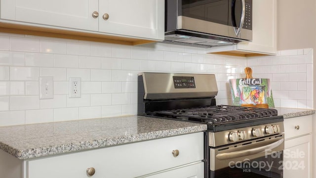 kitchen with stainless steel appliances, white cabinets, tasteful backsplash, and light stone countertops