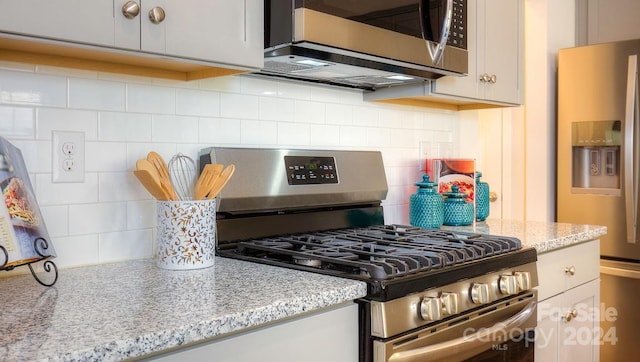 kitchen with stainless steel appliances, decorative backsplash, white cabinets, and light stone countertops