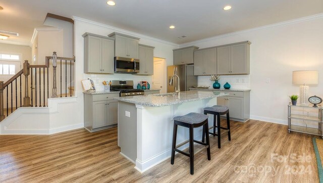 kitchen with appliances with stainless steel finishes, a kitchen breakfast bar, a kitchen island with sink, light wood-type flooring, and gray cabinetry